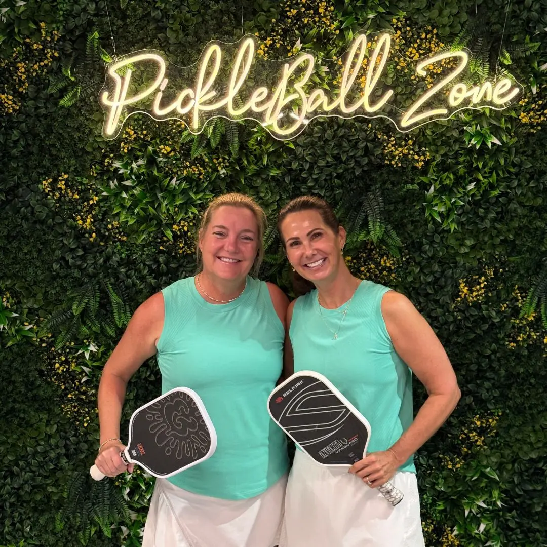 Two players with paddles under the Pickleball Zone neon sign