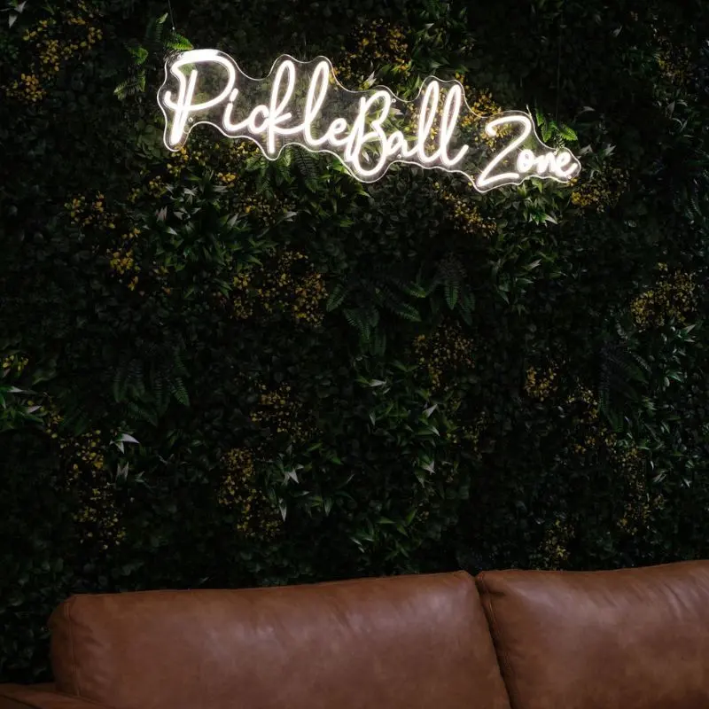 The Pickleball Zone neon sign on a green living wall